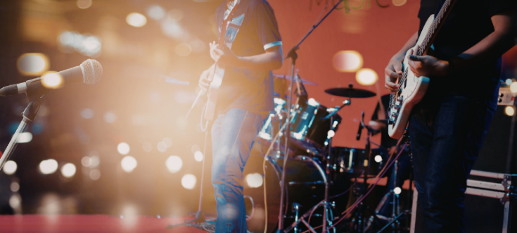 Zwei Gitarristen und ein Schlagzeuger performen auf einer festlich beleuchteten Hochzeitsbühne.