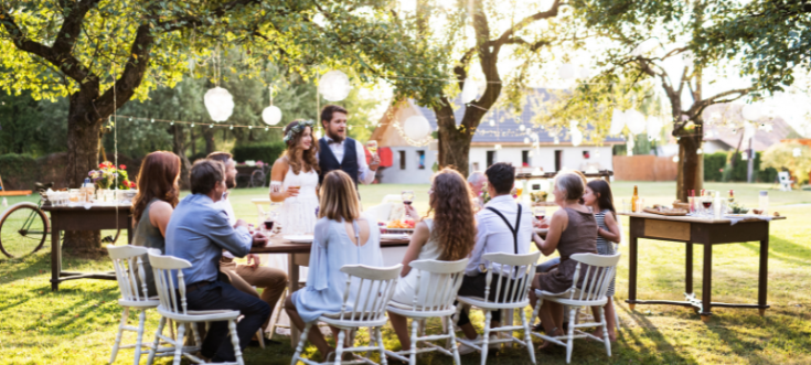 Brautpaar feiert mit Gästen an langer Tafel im Garten – mit Lichterketten und festlicher Stimmung.