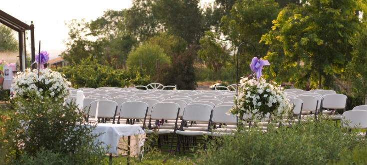 Outdoor-Trauung mit weißen Klappstühlen, Blumenarrangements und idyllischer Naturkulisse