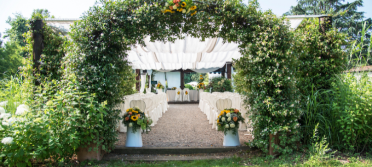 Outdoor-Hochzeitslocation mit blumengeschmücktem Traubogen, weißen Stühlen und romantischer Dekoration 