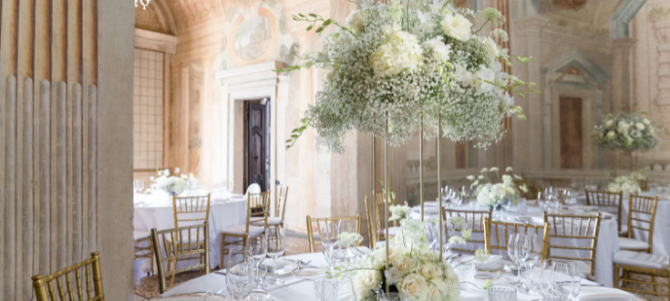 Prunkvoll dekorierter Hochzeitssaal mit weißen Tischdecken, goldenen Stühlen und üppigen Blumenarrangements